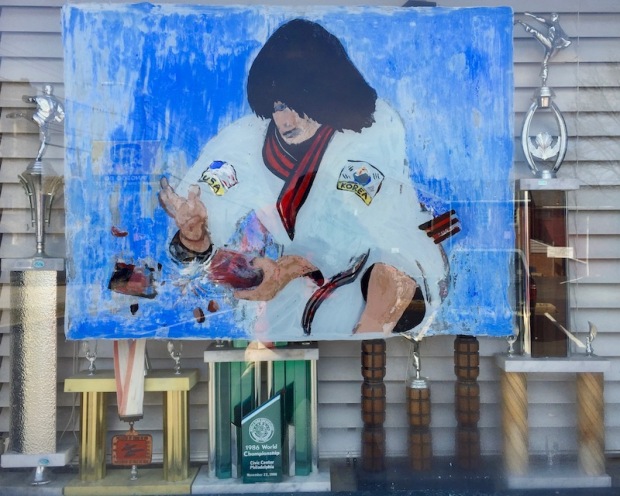 painting of karate student breaking a brick with his bare hand in window with trophies