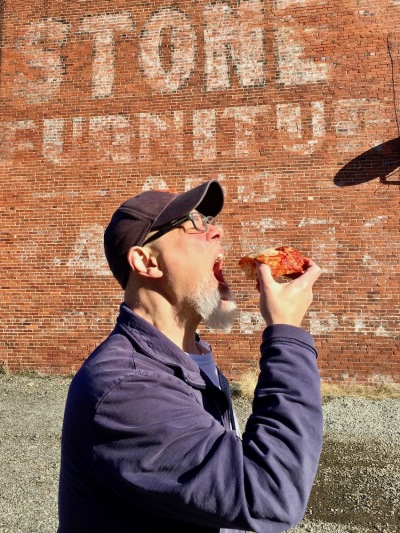 man holding pizza slice to his mouth outdoors