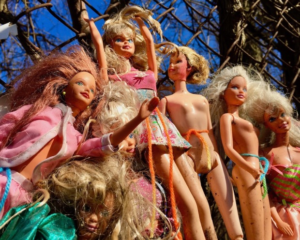 collection of Barbie dolls displayed on chain link fence in the sunshine