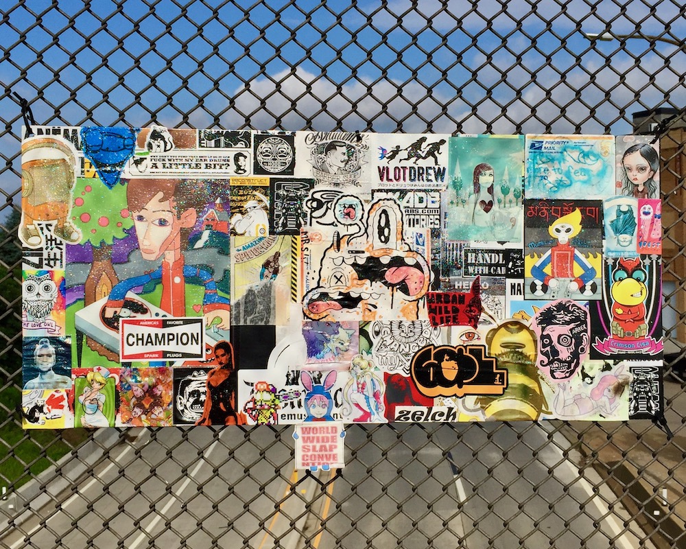 colorful collage of cartoon images, stickers, advertiments hung on chain link fence