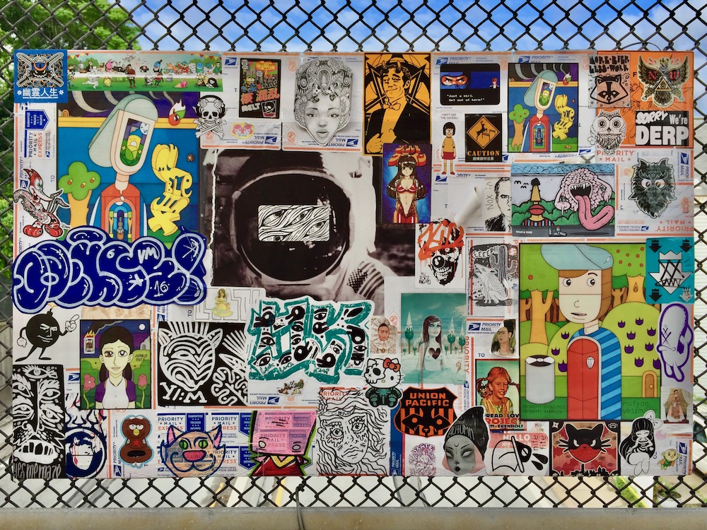 colorful collage of cartoon images, stickers, advertiments hung on chain link fence