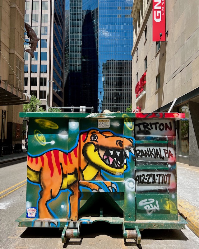 commercial dumpster painted with orange dinosaur