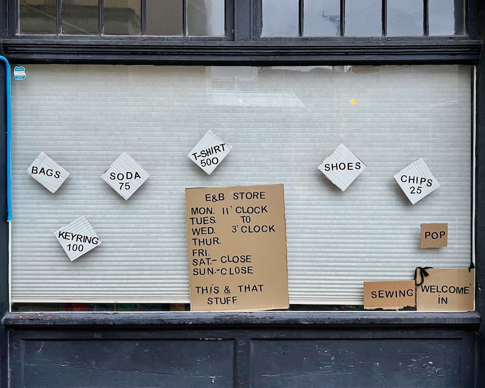 shop window with handmade signs for items on sale and store hours
