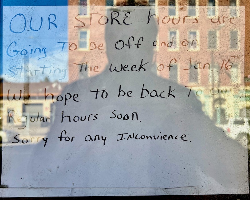 handwritten sign in shop window apologizing for irregular hours