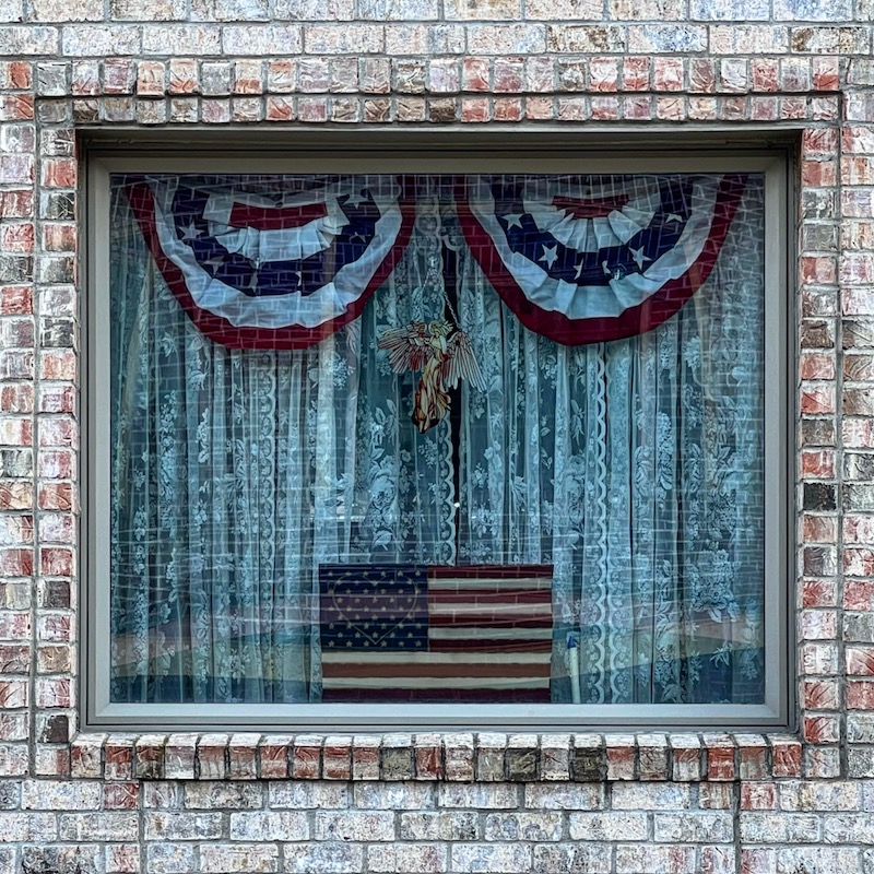 window in brick house decorated with American flag and bunting