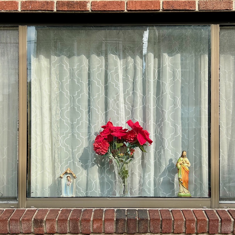 rowhouse window decorated with flowers in vase and statuette of Jesus