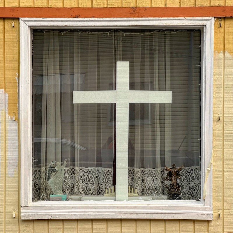 rowhouse window with large cross and small statuette of Jesus