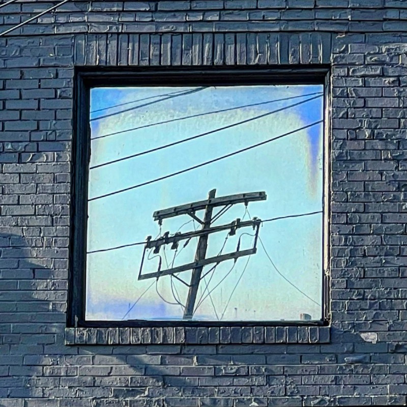 window in brick building reflecting sky and power lines