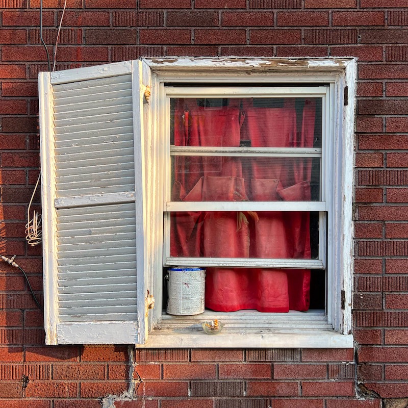 window with red curtain and paint can keeping window open