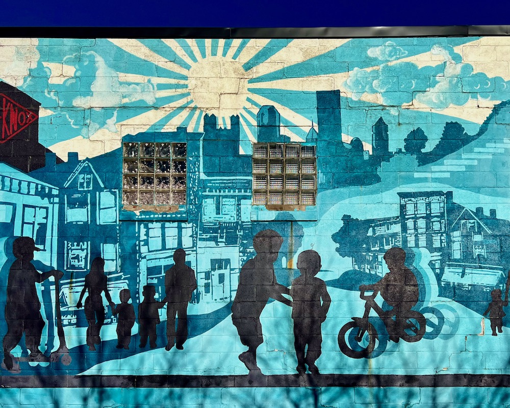 large mural on featuring skyline of downtown Pittsburgh with large sun in sky