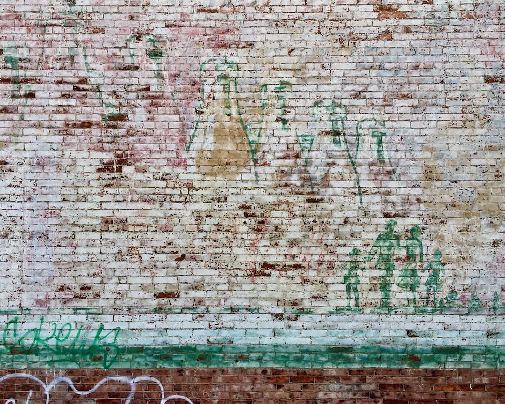 brick wall painted with faded advertisement including glass bottles