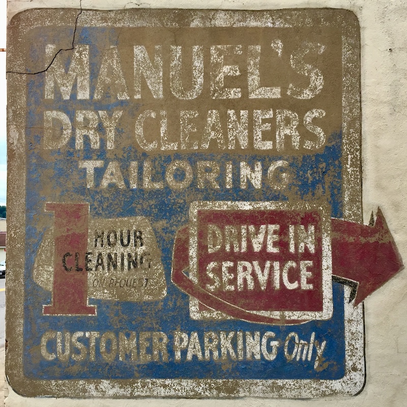 faded hand-painted sign for dry cleaners painted on brick wall