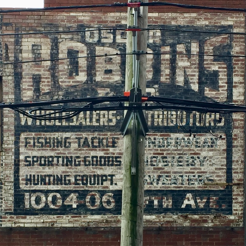 faded hand-painted sign for sporting goods store painted on brick wall