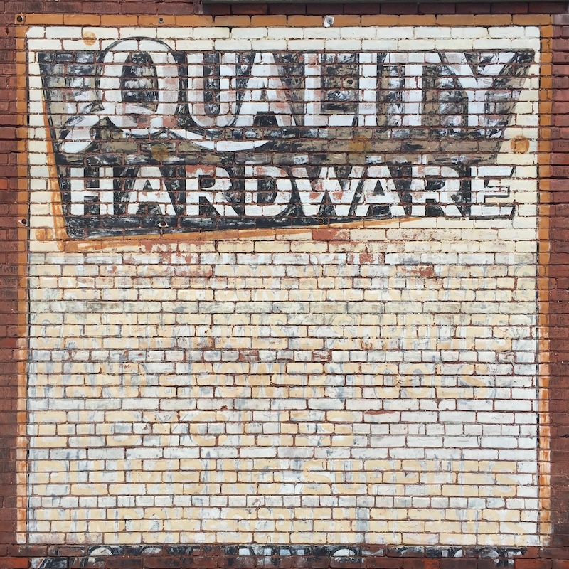 faded hand-painted sign for hardware store painted on brick wall